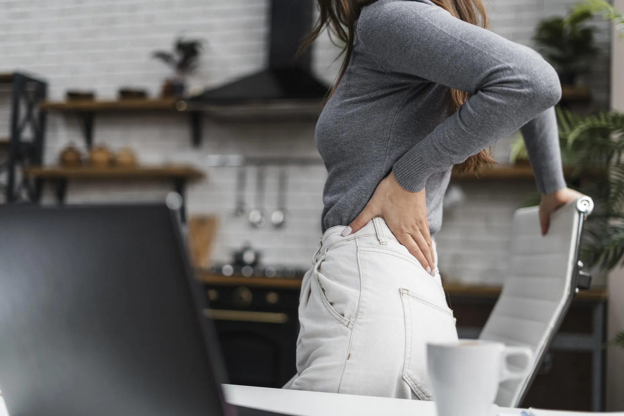Persona con dolor lumbar llevándose las manos a la zona baja de la espalda tras levantarse de una silla.