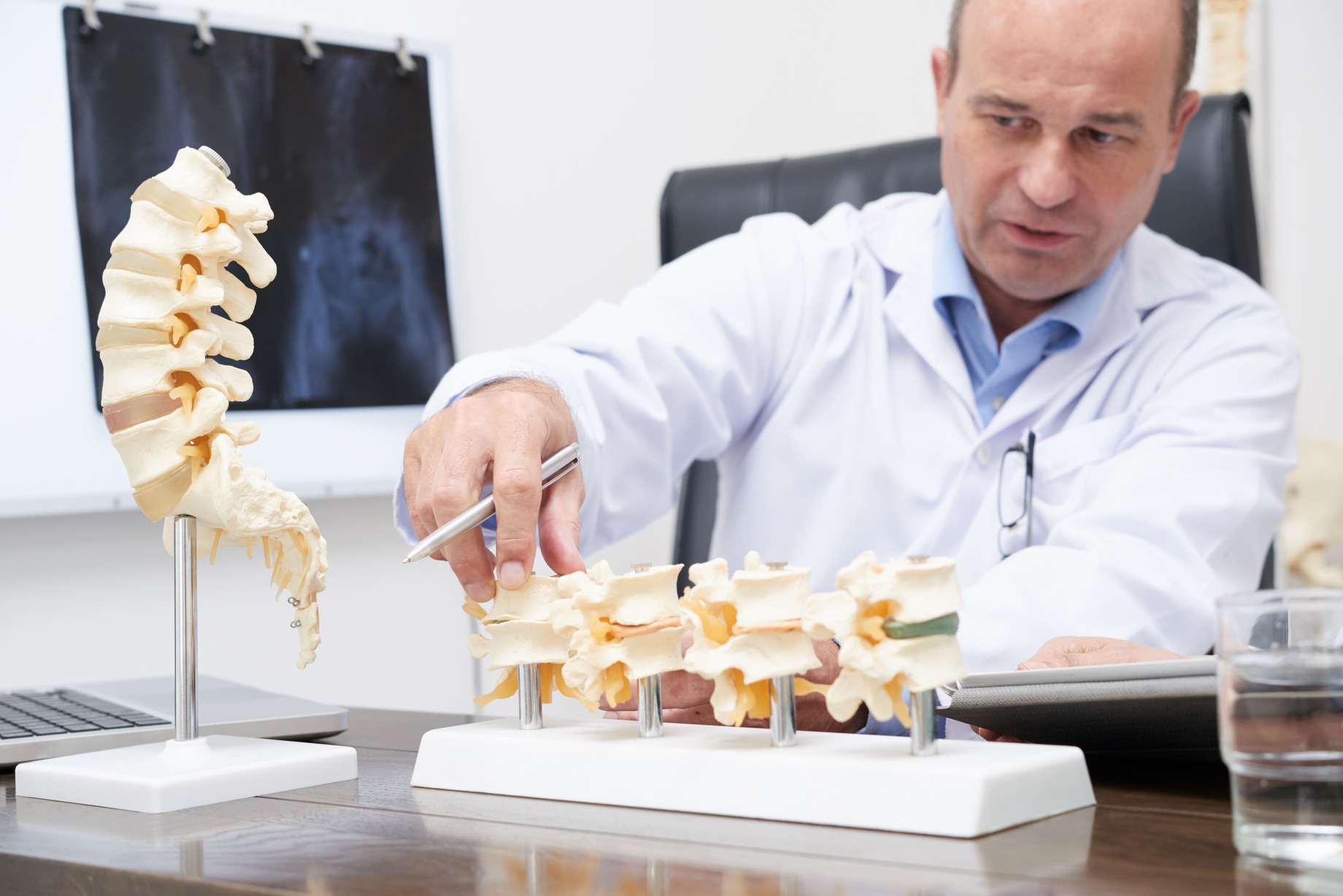 Fisioterapeuta especializado en osteoporosis mostrando modelo anatómico de vértebras para explicar el tratamiento con ejercicio terapéutico y magnetoterapia en clínica de Madrid. 